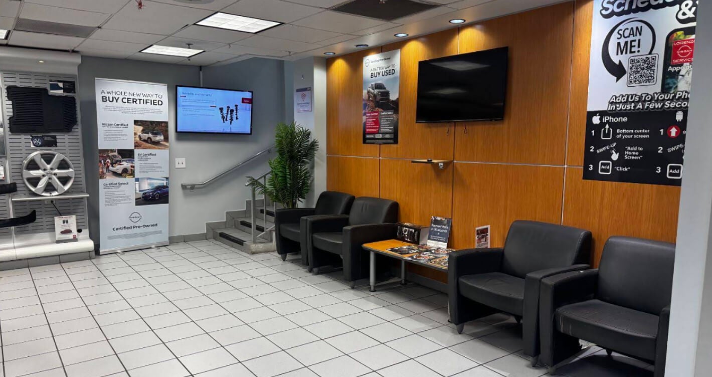 Interior view of the customer waiting area at Nissan Dealership Office featuring informational displays on Certified Pre-Owned programs.