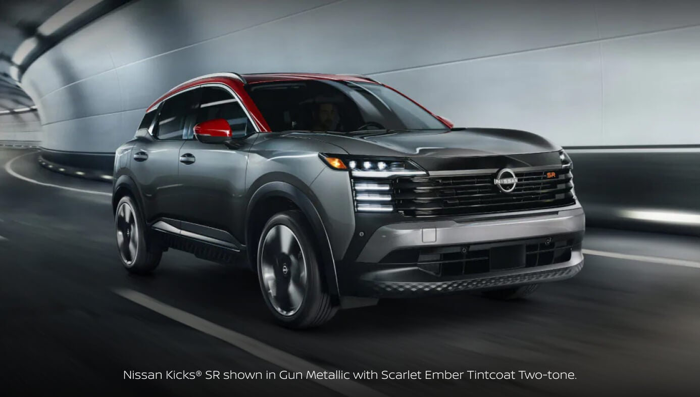 Front three-quarter view of a 2027 Nissan Kicks SR in Gun Metallic with Scarlet Ember Tintcoat Two-tone driving through a modern illuminated tunnel.