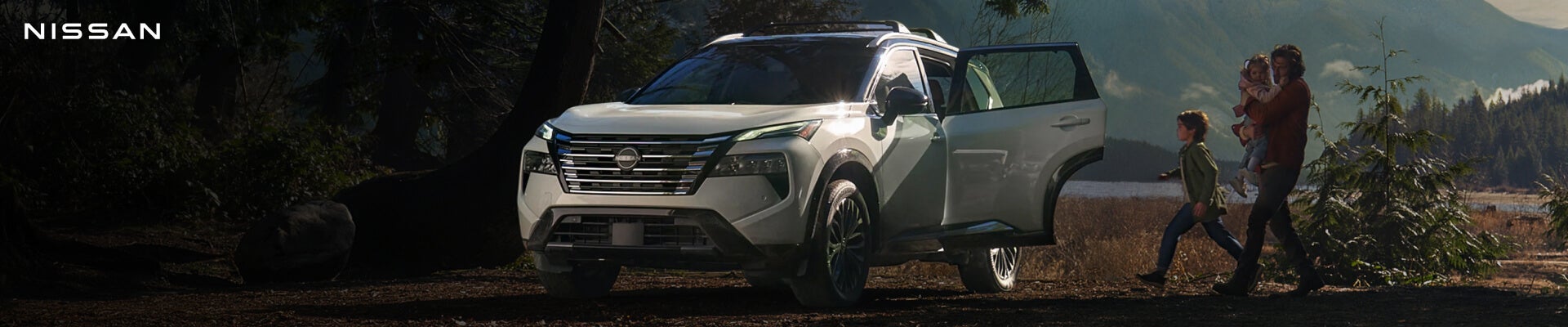 Three-quarter front view of a 2026 Nissan Rogue Platinum in Everest White Pearl alongside a family.