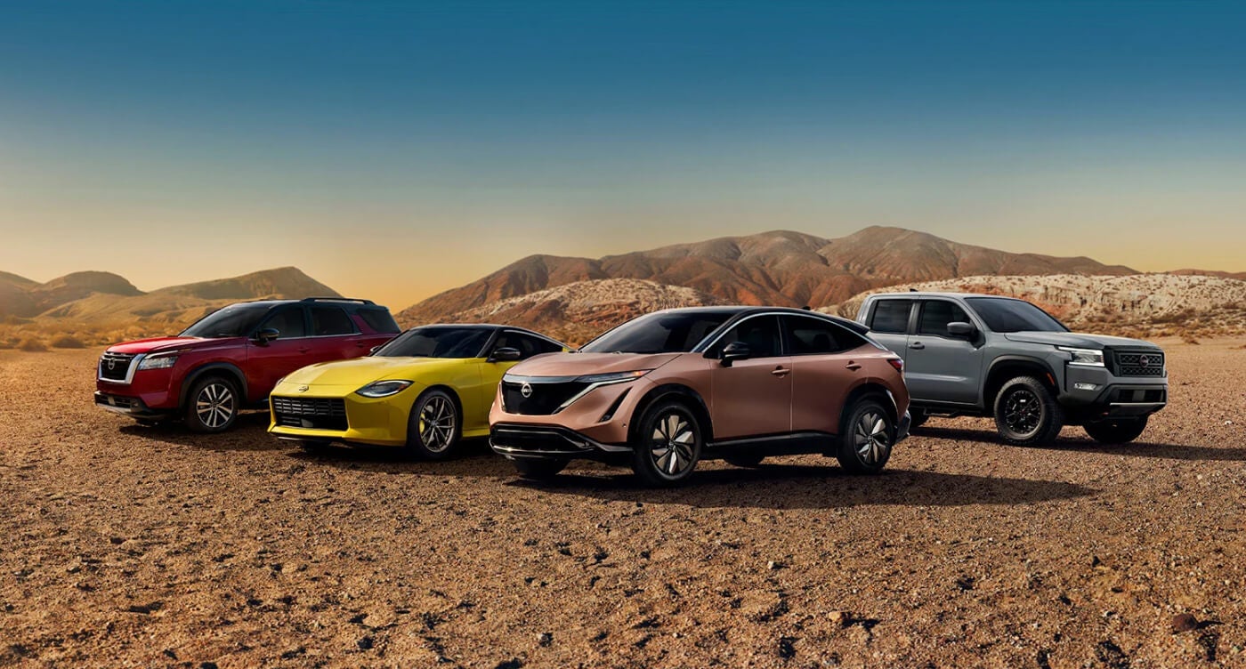 Lineup of 2024 Nissan vehicles in a variety of colors parked side-by-side in an open desert clearing.