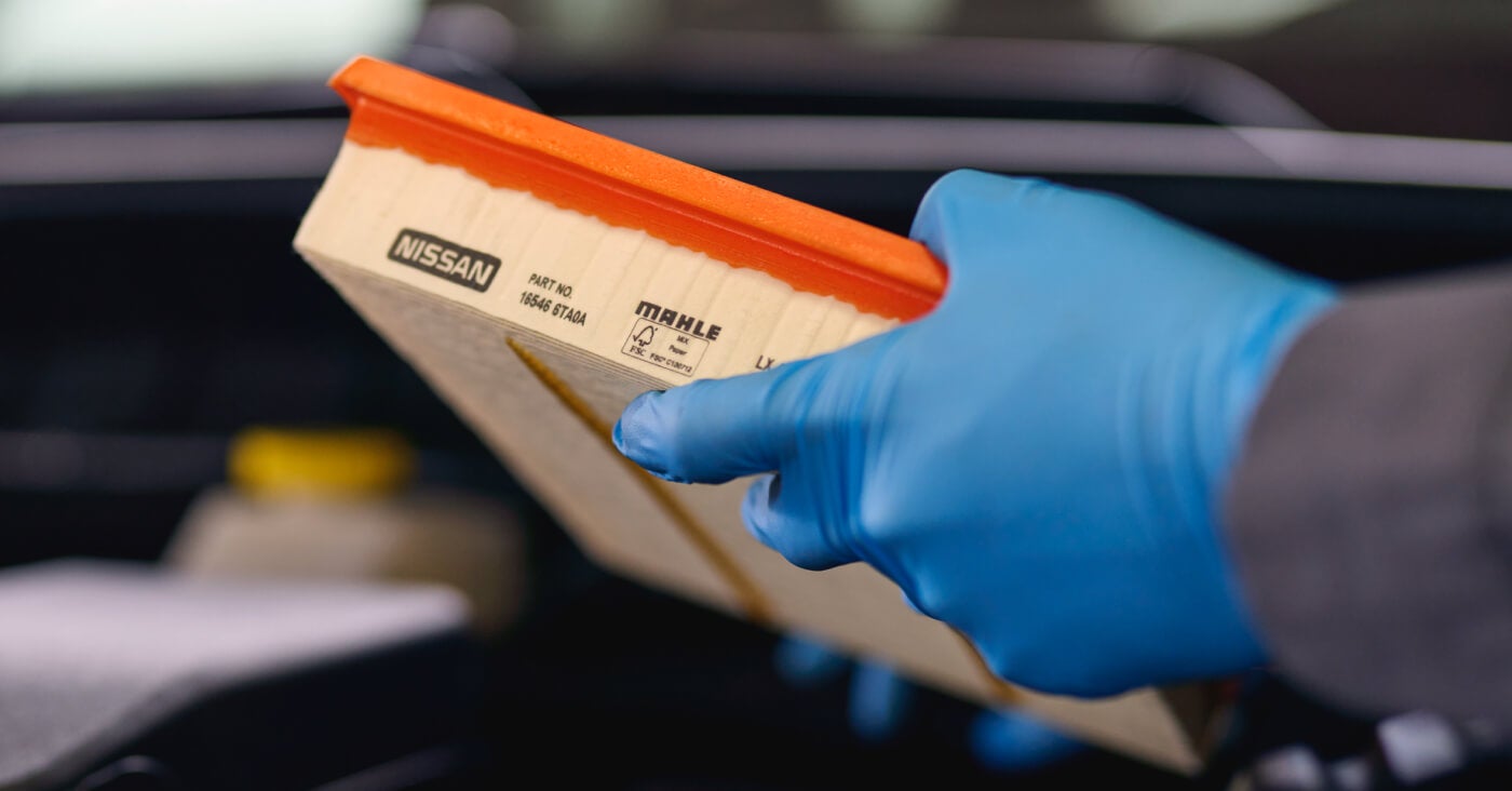 Close-up view of a certified technician holding a genuine Nissan engine air filter during routine vehicle maintenance.